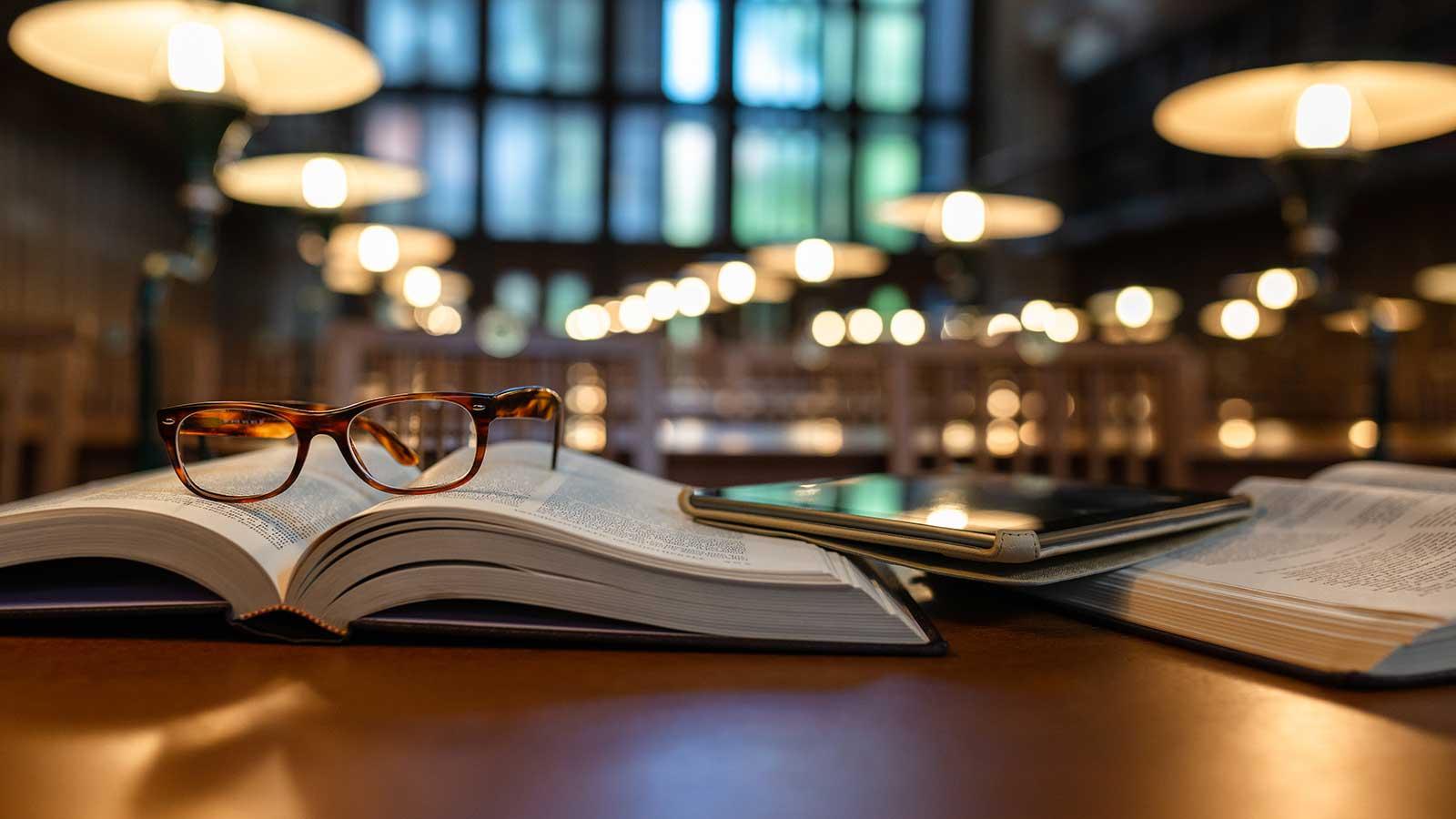 戴着眼镜和平板电脑在图书馆里看书，代表着自由教育和esball国际平台客户端